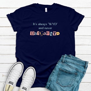 Op de afbeelding: Een marineblauw T-shirt met de tekst "It's always 'WYD' and never BagGaCoTD" gedrukt op de voorkant. De tekst is in een kleurrijke, uitgesneden stijl.
