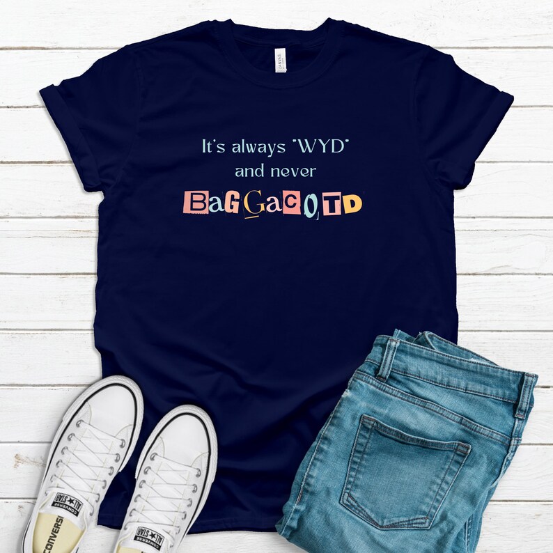 Op de afbeelding: Een marineblauw T-shirt met de tekst "It's always 'WYD' and never BagGaCoTD" gedrukt op de voorkant. De tekst is in een kleurrijke, uitgesneden stijl.