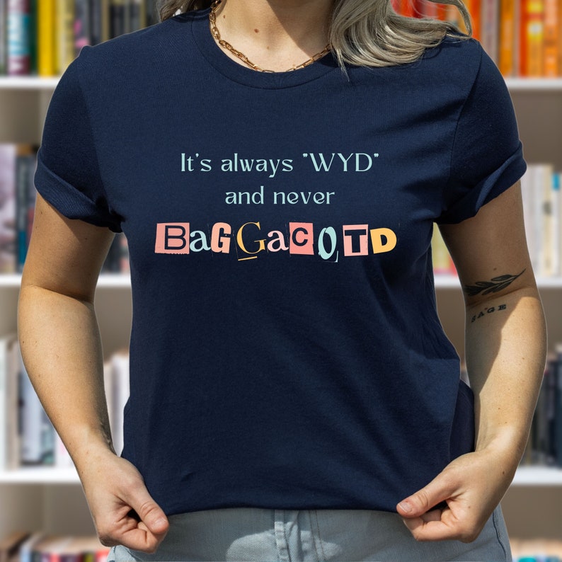 Op de afbeelding: Een marineblauw t-shirt met de tekst "It's always 'WYD' and never BagGaCoTD" gedrukt op de voorkant. De tekst is in een kleurrijke, uitgesneden stijl.
