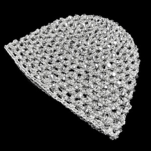 May include: A silver crocheted beanie hat with a delicate, open weave design. The hat is adorned with small, reflective embellishments, creating a shimmering effect. The hat is set against a black background.