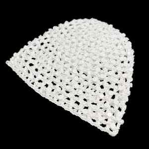 May include: A white crocheted beanie hat with an openwork pattern. The hat is made from a soft, textured yarn and has small, decorative beads. The hat is displayed against a black background.