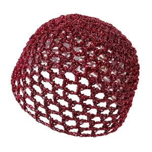 May include: A burgundy-colored crocheted hair net. The net is made of a shiny, metallic thread, and the open weave allows the background to be seen through it. The hair net is round and appears to be new.