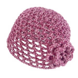 May include: A hand-knitted, open-weave hat in shades of pink and white. The hat features a floral embellishment on the side. The hat is made of a soft, textured yarn, perfect for cooler weather.