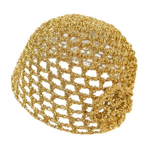 May include: A gold-colored, open-weave, crocheted head covering. The head covering is made of a metallic thread and has a net-like appearance. The item is likely a fashion accessory.