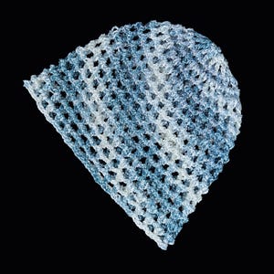 May include: A crocheted hat in a diamond shape, featuring a gradient of blue and white hues. The open weave design is visible, creating a textured appearance. The hat is set against a black background.