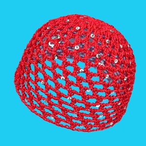 May include: A red crocheted cap with silver sequins. The cap is made of a net-like weave, and the sequins are evenly spaced throughout the design. The cap is a vibrant red color and is set against a bright blue background.