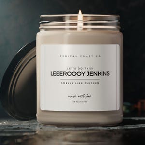 Peut inclure: Une bougie en verre dans un bocal avec une étiquette blanche sur laquelle est inscrit "CYNICAL CRAFT CO", "LET'S DO THIS! LEEEROOOY JENKINS", "SMELLS LIKE CHICKEN", "made with love", "50 hours/9 oz".