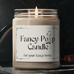 May include: A beige candle in a glass jar with a white label that reads "Fancy Poop Candle for your fancy home". The label has a decorative border and a small illustration of a top hat and a mustache.