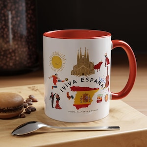 May include: A white ceramic mug with a red interior and handle, featuring colorful illustrations of Spanish landmarks, a map of Spain with its flag, a soccer player, dancers, and the text ¡VIVA ESPAÑA! FIESTA, FLAMENCO & FLAVOR printed on the front.