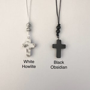 May include: Two necklaces with cross pendants. The necklace on the left has a white howlite cross and white beads. The necklace on the right has a black obsidian cross and black beads.