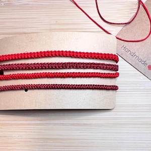 May include: Four strands of red and burgundy cord on a brown card with the text "Handmade with love".