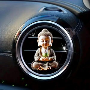 May include: A small, beige figurine of a meditating Buddha holding a green lotus flower. The figurine is placed in a car's air vent.