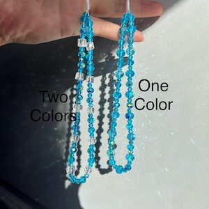 May include: Two beaded phone charms in the image. One charm is a single strand of blue beads, and the other has a mix of blue and clear beads. The charms are strung on white cords. The text "Two Colors" and "One Color" are visible.