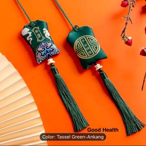 May include: Two green decorative pouches with long tassels. One pouch features embroidered clouds and text, the other has a gold emblem and text. The tassels are a darker green. The text "Good Health" is visible.