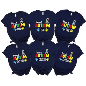 May include: Navy blue t-shirts with the text "Proud Autism" in red and yellow, a colorful ribbon, and the words "Mom", "Bro", "Dad", "Custom", "Cousin", and "Friend". Each shirt has a handprint design.