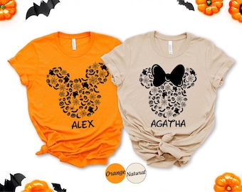 May include: Two short-sleeved t-shirts, one orange and one natural, featuring a Halloween-themed Mickey Mouse head design. The design is filled with bats, spiders, and pumpkins. The orange shirt says "ALEX" and the natural shirt says "AGATHA".