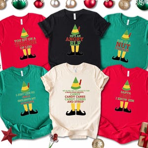 May include: A collection of six colorful t-shirts with elf-themed designs. Each shirt features a different color and a humorous text graphic, including phrases like "You Sit on a Throne of Lies" and "He's an Angry Elf."