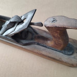 May include: An antique wooden hand plane with a metal blade and handle. The plane has a weathered appearance, with visible wear and tear on the wood and metal components. The handle is a dark brown color.