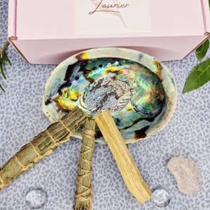 Może przedstawiać: Zestaw trzech patyczków do kadzidła, w tym biała szałwia, palo santo i rozmaryn, ułożone są w zielonej muszli abalonu. Muszla leży na szarej i białej powierzchni z wzorem.