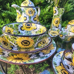 Może przedstawiać: Zestaw ceramicznych naczyń w stylu słonecznika, w tym czajnik, cukiernica, dzbanek do śmietanki, wazon i miski. Naczynia są białe z żółtym i zielonym wzorem słonecznika.