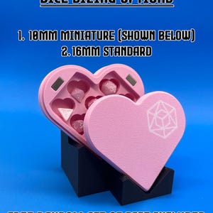 May include: Pink heart-shaped dice tray with a black stand. The tray has a compartment for dice and a lid with a heart-shaped cutout. The lid has a white design of a d20 die.  "DICE SIZING OPTIONS" is written at the top of the image.  "1. 10MM MINIATURE (SHOWN BELOW)" and "2. 16MM STANDARD" are written below the title.  "FREE RANDOM SET OF DICE INCLUDED" is written at the bottom of the image.