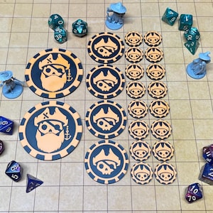 Può includere: Una collezione di accessori da gioco che include due grandi gettoni circolari con un design a teschio pirata, quattro gettoni medi e sedici piccoli gettoni con un'icona a teschio. Include anche vari dadi poliedrici e due piccole statuette blu.