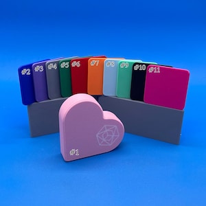 May include: A set of 11 colour swatches, numbered 1 through 11, with a pink heart-shaped object in the centre. The heart has a white geometric design and the text '#1' on it.