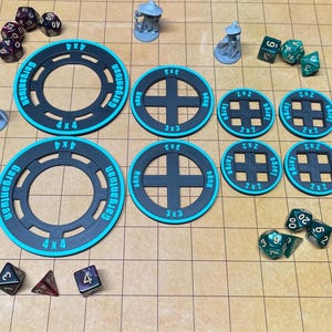 May include: A selection of tabletop gaming accessories, including dice, miniature figurines, and circular and square game board tiles. The tiles are black with teal accents and feature size designations like "4x4" and "2x2".