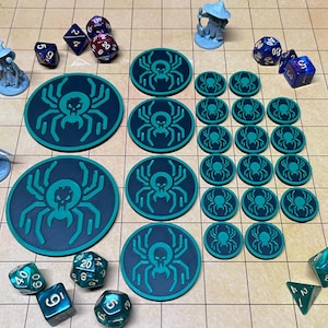 May include: A collection of tabletop gaming accessories, including dice and tokens. The tokens are dark blue with a teal spider design. Several miniature figurines are also present, along with various multi-sided dice in shades of blue, purple, and teal.