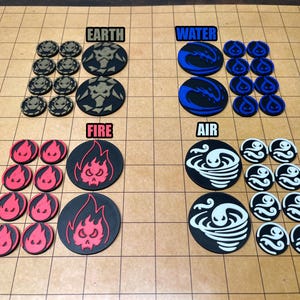 May include: A collection of game tokens, each representing an element: Earth, Water, Fire, and Air. The tokens are black, blue, red, and white, with detailed designs. The tokens are arranged on a grid-patterned surface.