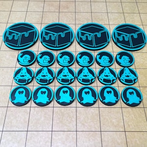 May include: A collection of black and teal game tokens. The tokens feature various designs, including a cube with dripping lines, a monster face, a wizard, and a ghost. The tokens are arranged on a grid.
