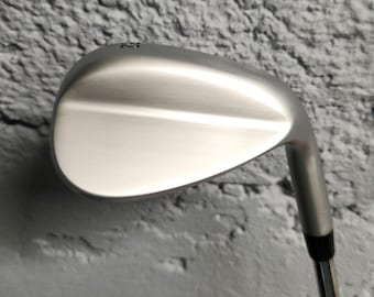 May include: A silver-colored golf wedge club head with a smooth, matte metallic finish. The club head features a curved, teardrop-shaped face and a hosel that connects to a thin, cylindrical metal shaft. The number 58 is engraved on the top.