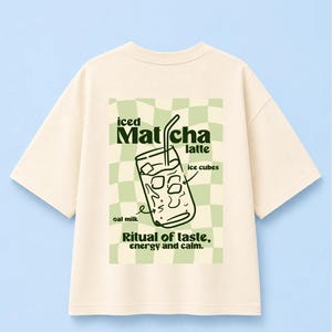 Könnte beinhalten: Ein cremefarbenes T-Shirt mit einer Grafik auf der Rückseite auf hellgrün kariertem Hintergrund. Die Grafik zeigt ein Glas Eismatcha-Latte mit dem Text: iced Matcha latte, ice cubes, oat milk, Ritual of taste, energy and calm.