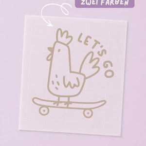 Könnte beinhalten: Ein quadratischer, halbtransparenter Bügeltransfer mit einer hellbraunen Strichzeichnung eines Huhns auf einem Skateboard. Der Text "LET'S GO" steht neben dem Huhn. Ein violettes rechteckiges Etikett trägt die Aufschrift "ERHÄLTLICH IN ZWEI FARBEN".