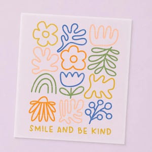 Könnte beinhalten: Ein rechteckiges weißes Blatt mit einem Raster aus farbenfrohen Strichzeichnungen, darunter Blumen, Blätter, abstrakte Formen und ein Regenbogen. Der Text "SMILE AND BE KIND" ist in gelben Großbuchstaben am unteren Rand aufgedruckt.