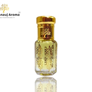 Pode incluir: Um pequeno frasco de vidro transparente com uma tampa dourada e desenhos dourados intrincados. O frasco está cheio de um líquido amarelo claro. O frasco é etiquetado com "A Kannauj Aroma" com o lema "Enhance Your Personality".