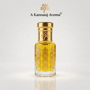 May include: A clear glass perfume bottle with a gold cap and a yellow liquid inside. The bottle features an intricate gold geometric pattern on its sides. Above the bottle, the text A Kannauj Aroma is printed with a gold tree icon above it.