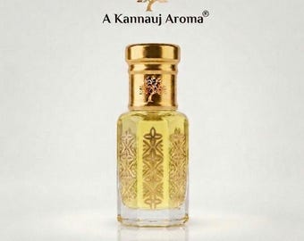 May include: A clear glass perfume bottle with a gold cap and a gold-toned metallic base featuring an embossed floral pattern. The bottle contains a pale yellow liquid. Above the bottle, the text A Kannauj Aroma is printed in black.