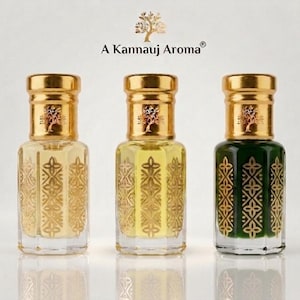 Könnte beinhalten: Drei Glasparfümflaschen mit goldenen Verschlüssen und goldenen geometrischen Mustern. Jede Flasche zeigt ein goldenes Baumlogo und den Text A Kannauj Aroma. Die Flüssigkeiten im Inneren sind jeweils farblos, hellgelb und dunkelgrün.