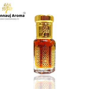 Puede incluir: Una pequeña botella de vidrio transparente con una tapa dorada y un diseño dorado. La botella está llena de un líquido marrón oscuro. La botella está etiquetada con "A Kannauj Aroma" y "Enhance Your Personality".