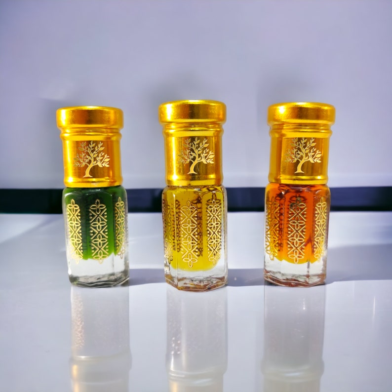 May include: Three small glass bottles with gold lids and labels. The bottles contain a green, yellow, and orange liquid. Each label features a gold tree design.