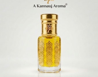 May include: A clear glass perfume bottle with a gold-colored cap and base, featuring an intricate embossed geometric pattern on the sides. The bottle contains a yellow liquid and is labeled with the text A Kannauj Aroma and a tree icon.