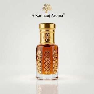 May include: A glass perfume bottle filled with amber liquid, featuring a gold cap with a tree emblem and gold geometric patterns on the sides. Above the bottle, the text A Kannauj Aroma is displayed with a gold tree icon centered above it.