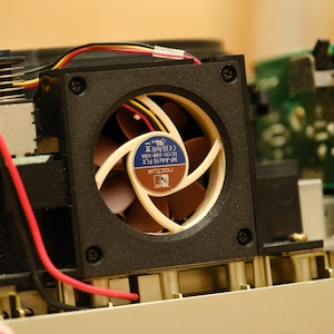 May include: Close-up of a black computer fan with a brown and white blade. The fan has a blue label with the text "Noctua NF-A4x10 FLX DC12V 0.13A-0.05A CE RoHS" on it.