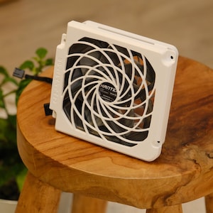 May include: A white computer fan with a black fan blade and a white protective grill. The fan is square and has the brand name "HANTEC" visible on the center label. The fan is sitting on a wooden stool.