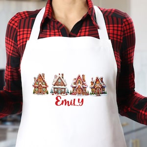 May include: White Christmas-themed apron with a row of four gingerbread houses and the name "Emily" printed in red.