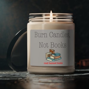 May include: A white candle with a gray label that reads "Burn Candles, Not Books" and "read banned books". The label also features a stack of books with a blue and orange cover.
