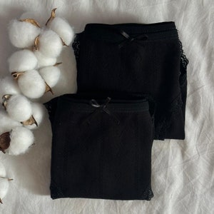 May include: Two pairs of black underwear with lace trim. Each pair has a small black bow on the front.