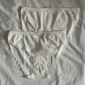 May include: Two pairs of white cotton underwear with lace trim. The underwear has a striped pattern.