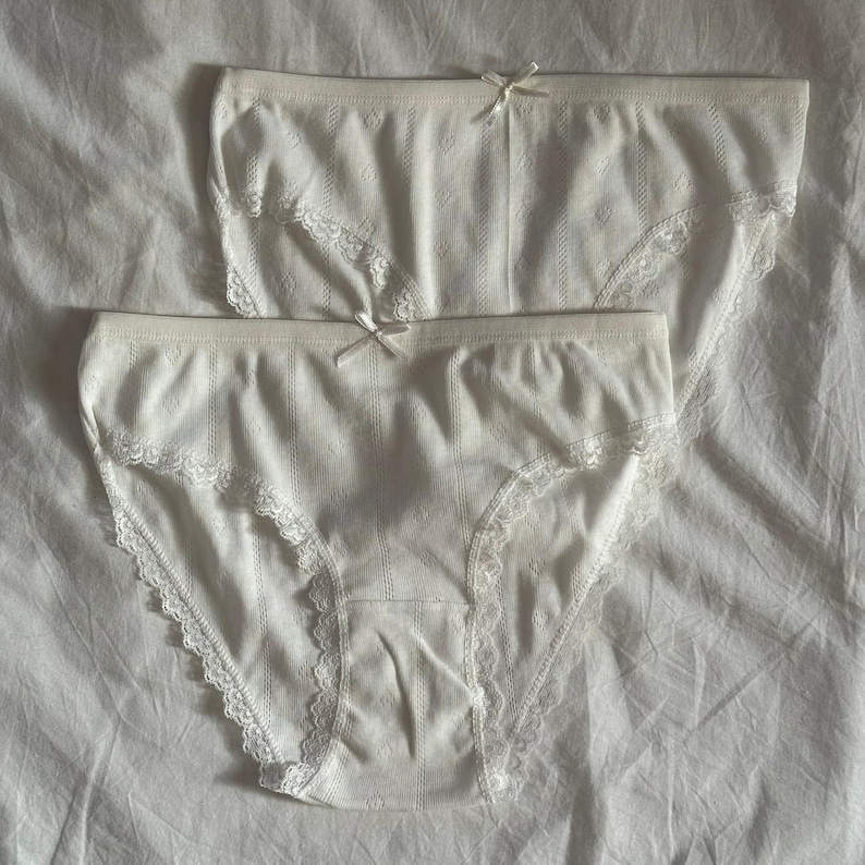 May include: Two pairs of white cotton underwear with lace trim. The underwear has a striped pattern.